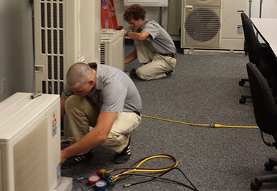 Two Benchmark Service technicians maintaining and servicing a ductless ac system in Dallas-Fort Worth.